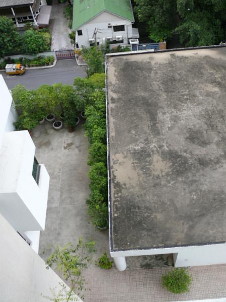 P1000024.JPG - The northern wall (on the left of our condo), the covered entrance (lower end of the photo).

The potted trees line a shady enclave well suited for working with a laptop.

The path to the pool is to the left of our condo (just under the windows of the tall condo building on the right).